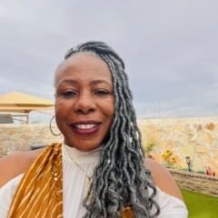 A woman with long grey hair and a yellow top.